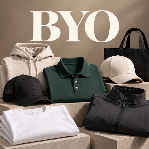 A styled assortment of apparel and accessories arranged on stone blocks against a warm beige background, with large 'BYO' text at the top. Visible items include a cream hoodie, dark green polo shirt, black trucker cap, cream baseball cap, black zip jacket, white T-shirt, and a black tote bag.
