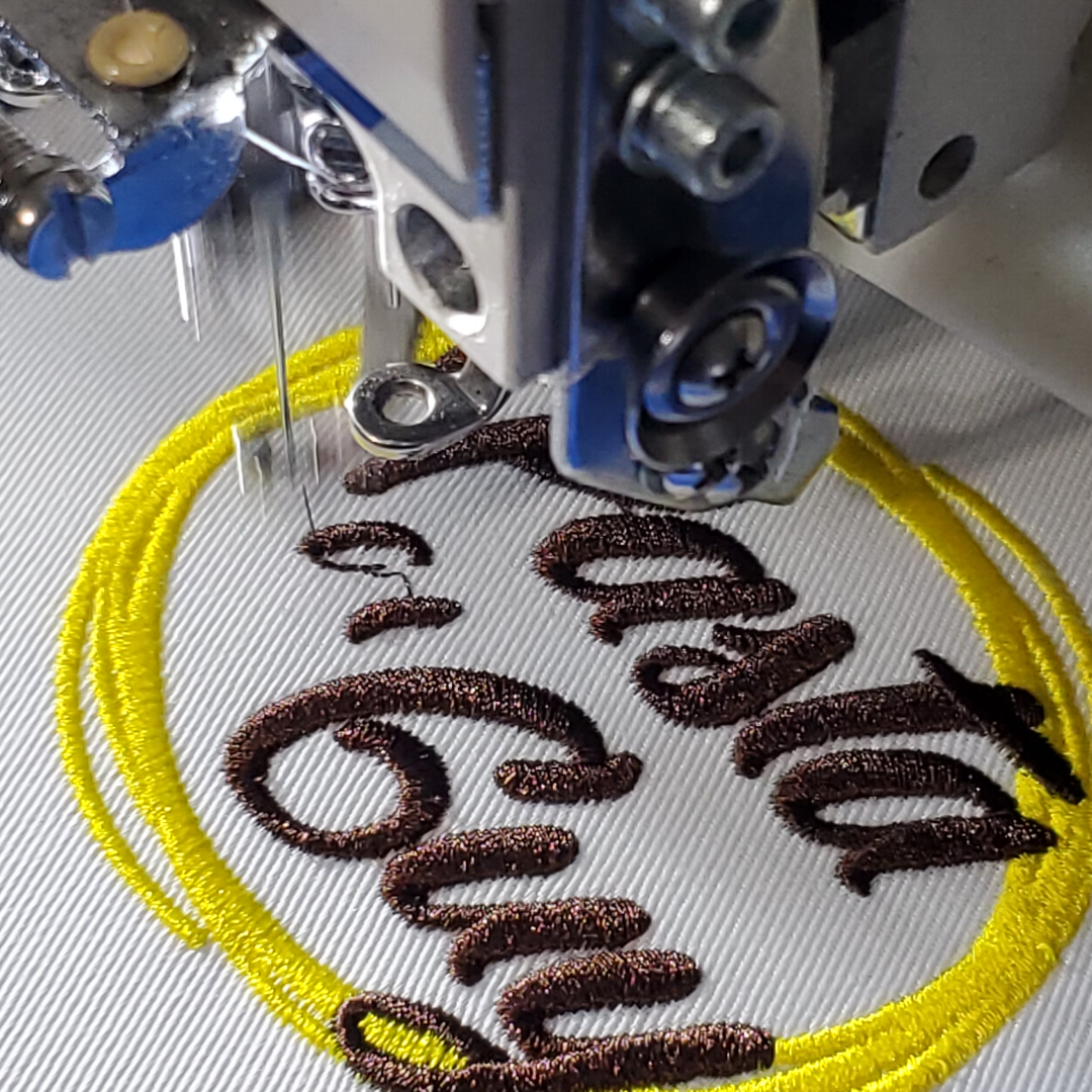 Embroidery machine stitching text and a yellow circle on fabric